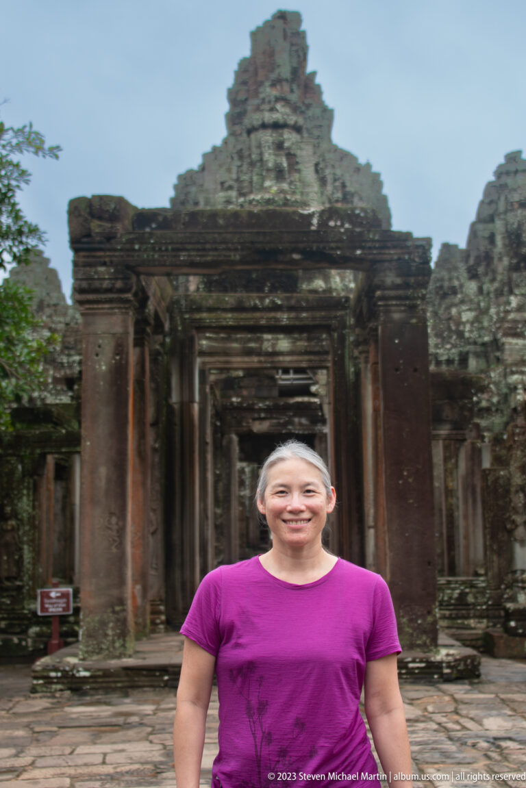 Female visitor in a magenta shirt standing before a sandstone doorway at Bayon Temple.