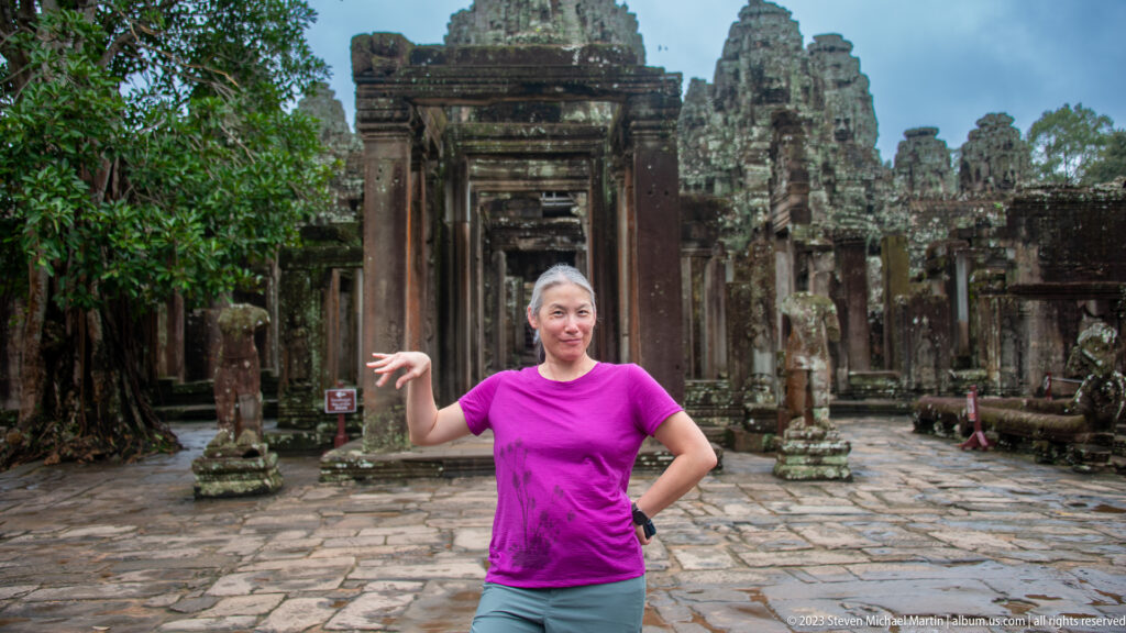 Female visitor in a magenta shirt posing before a Bayon Temple doorway.