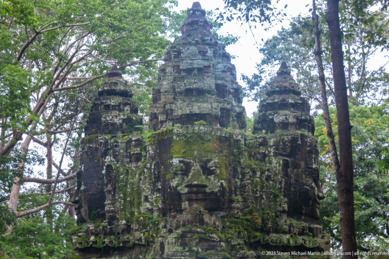 Close view of several moss-covered monumental faces on an Angkor Thom gate tower.