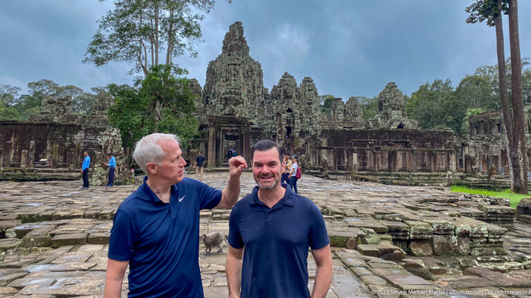 Two male visitors interacting playfully in front of Bayon Temple's central sanctuary.