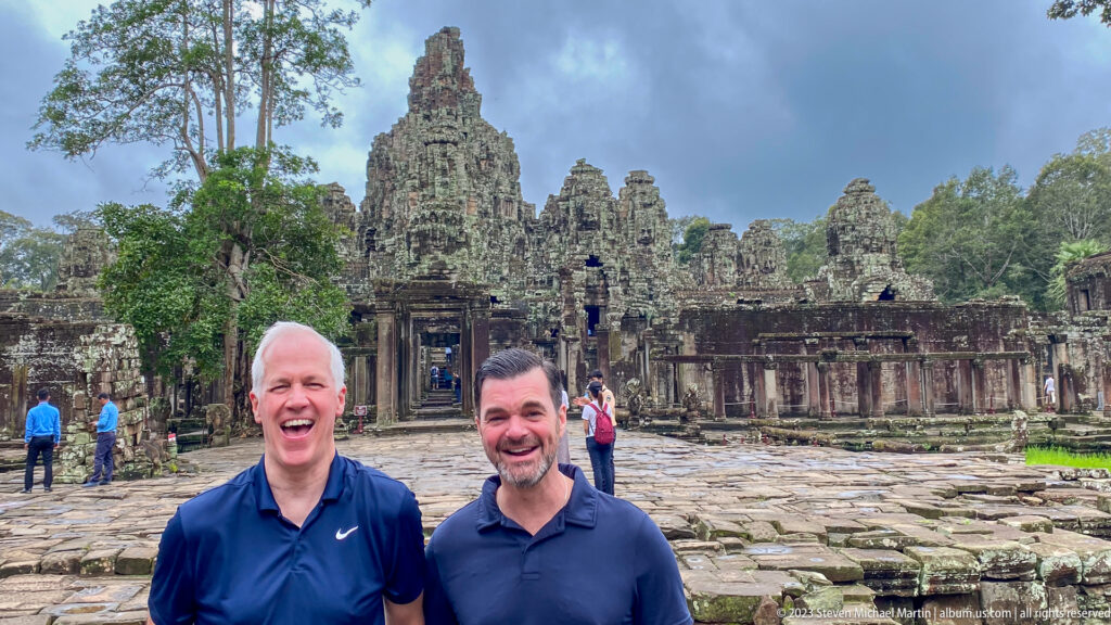 Two laughing male visitors posing close to the camera with Bayon Temple behind them.