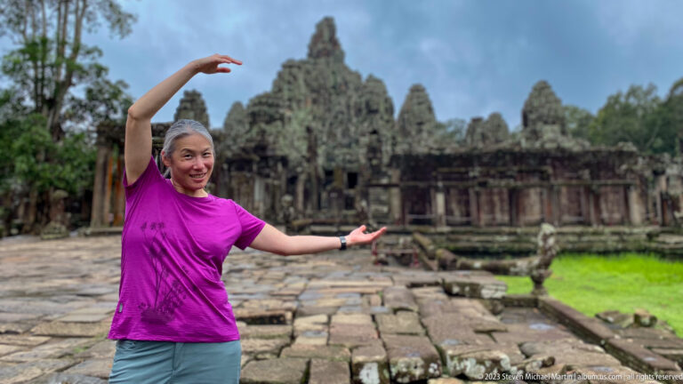 Female visitor in a magenta shirt gesturing toward Bayon Temple's central towers.