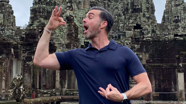 Close portrait of a male visitor gesturing in front of Bayon Temple's towers.