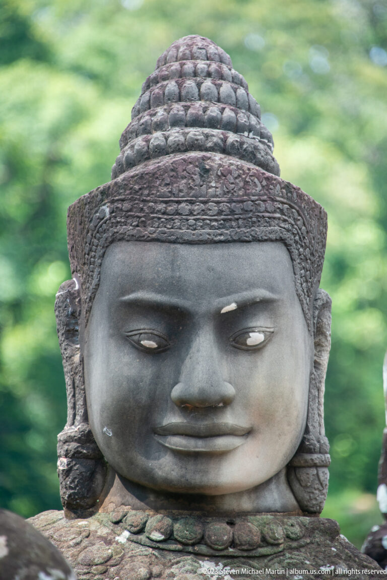 Centered sandstone guardian head with rounded patterned headdress and calm expression.