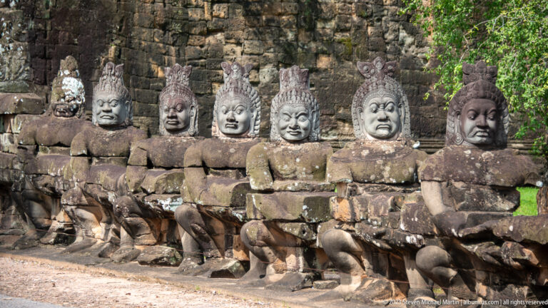Seven seated stone guardians in a row, each with a different weathered face and headdress.