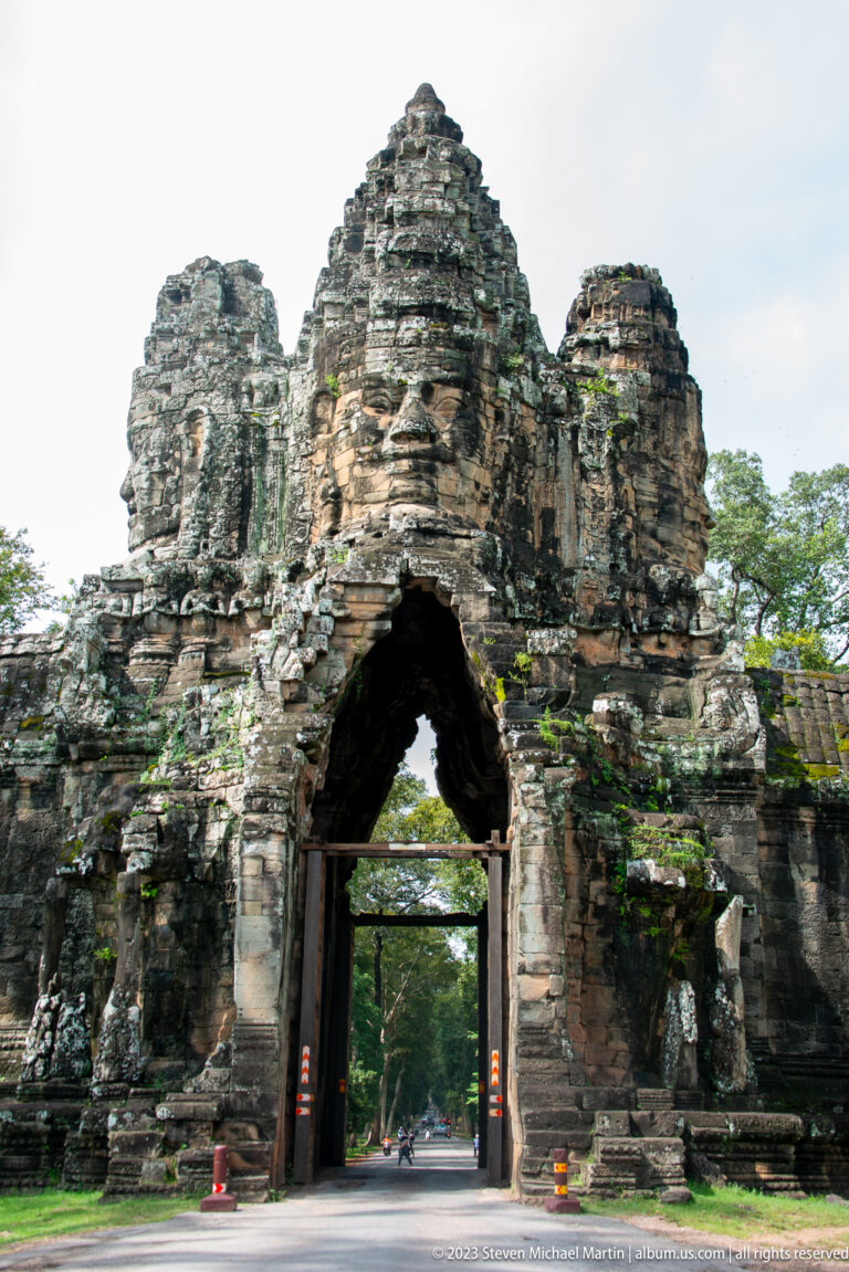 Monumental Angkor Thom stone gate with pointed arch spanning a roadway.
