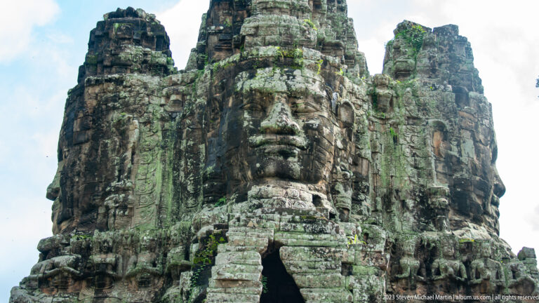 Low-angle view of a carved face tower above a narrow stone doorway.