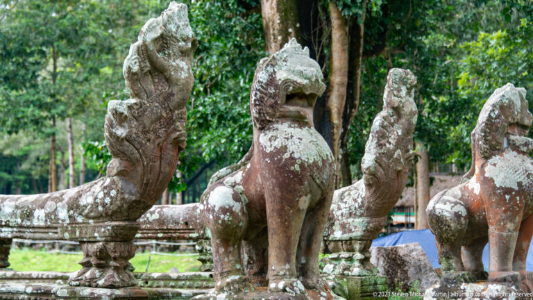 Row of lichen-covered stone guardian animals with raised heads and open mouths.