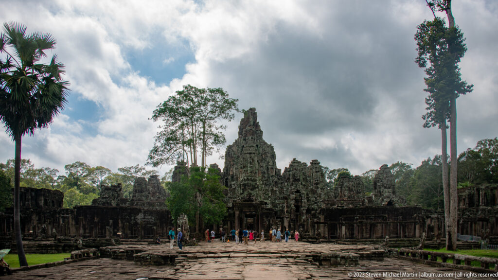 Wide stone courtyard leading toward Bayon Temple under dark clouds.