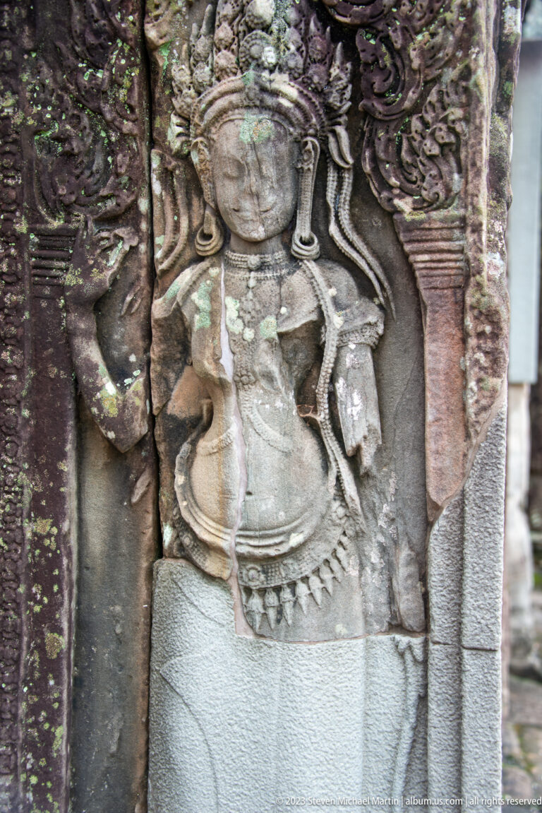 Standing Khmer female deity relief with elaborate hair and jewelry.