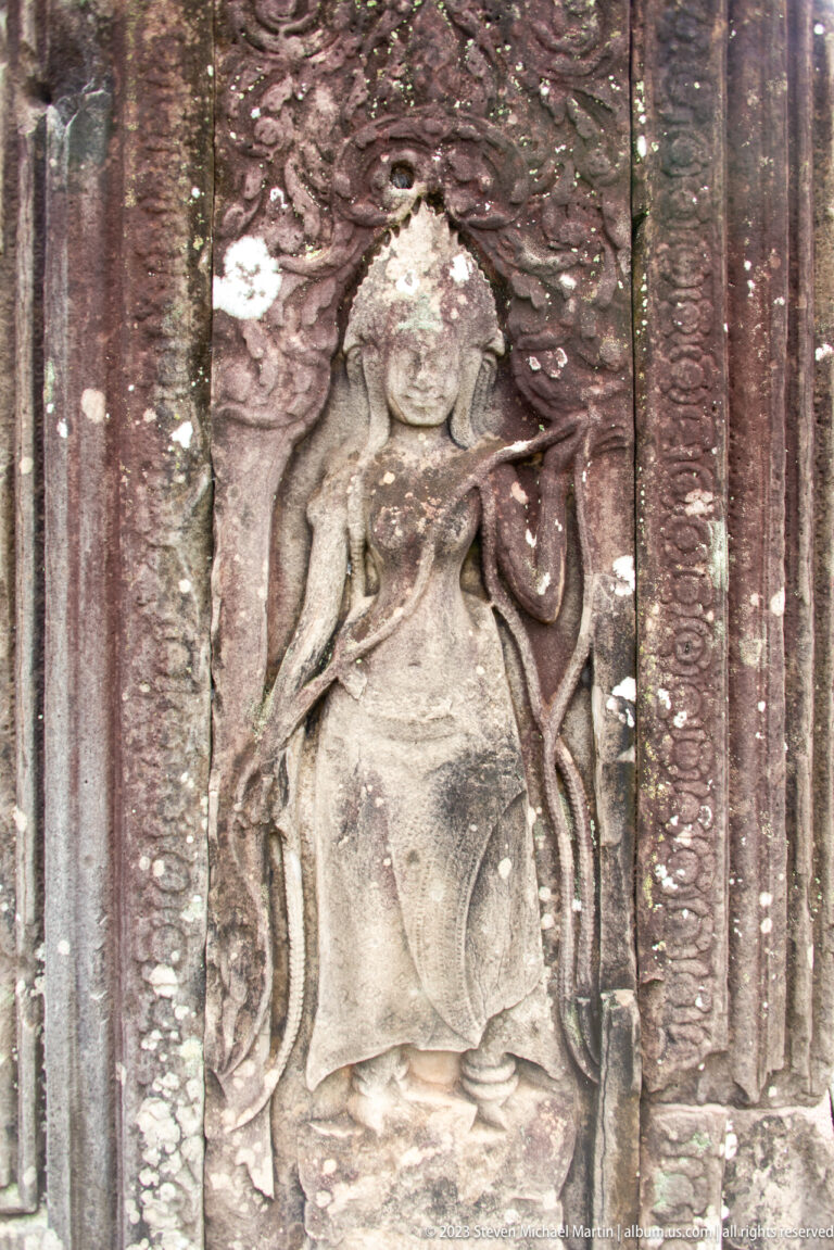 Weathered standing female deity carved in a narrow stone panel.