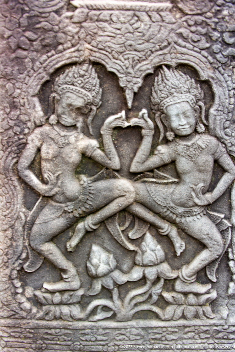 Two carved female figures facing each other above fish and flowing water motifs.