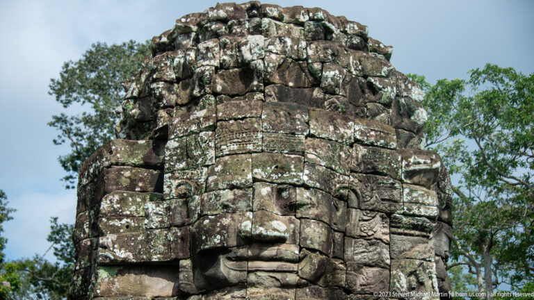 Close view of a serene carved face on a lichen-covered Bayon tower.