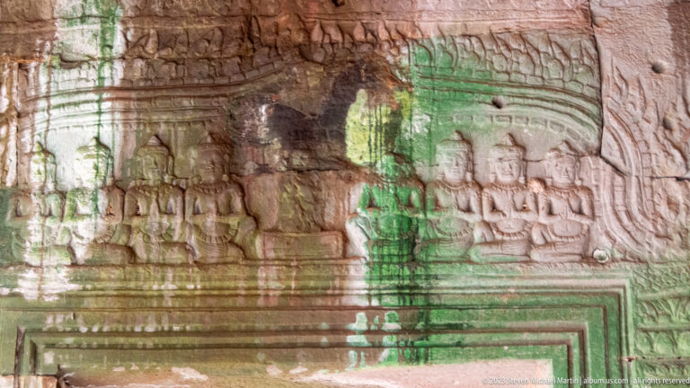 Carved seated figures and shrine forms crossed by bright green pigment streaks.