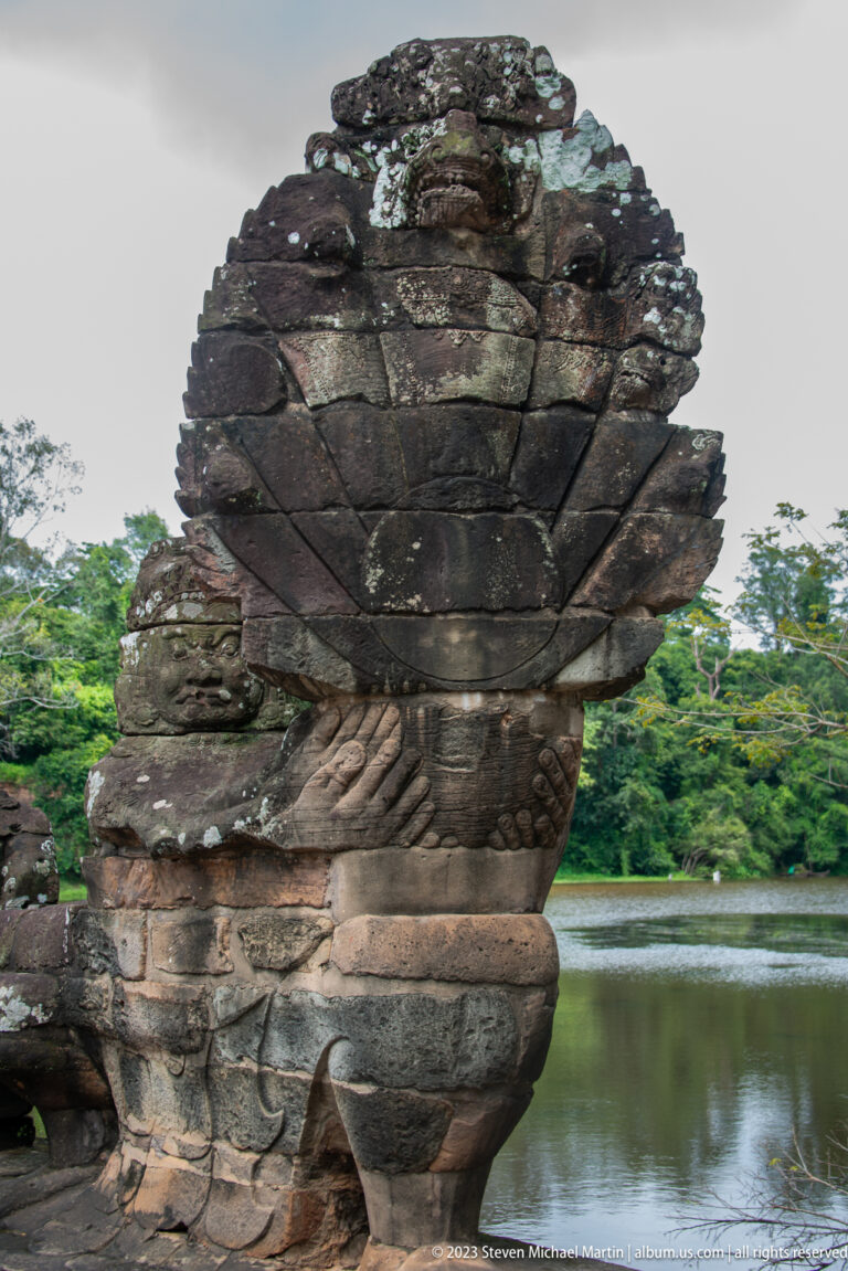 Weathered multi-headed stone naga terminal seen in profile beside the green moat at Angkor Thom.