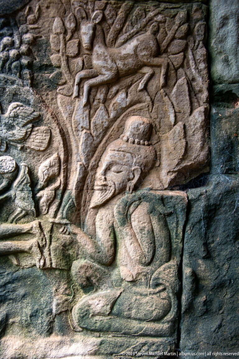 Close stone relief of a crouching figure beneath overlapping carved bodies.