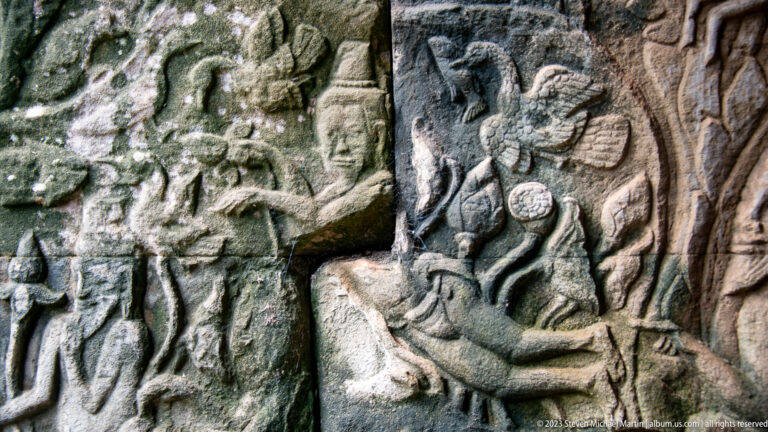 Khmer bas-relief with a seated figure surrounded by attendants and ceremonial objects.