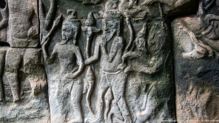 Close stone relief of overlapping standing figures, including one with both arms raised.