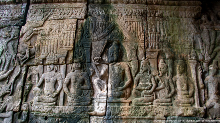 Khmer stone relief with a central seated figure beneath a canopy and attendants on both sides.