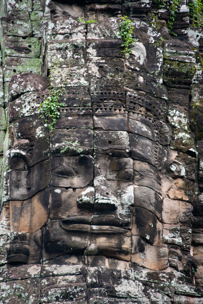 Large serene face carved across weathered sandstone tower blocks.