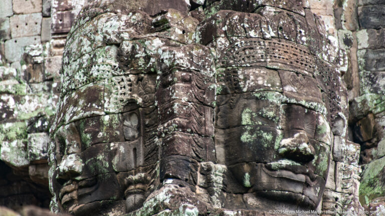 Three monumental carved faces on adjoining sides of a weathered Bayon tower.