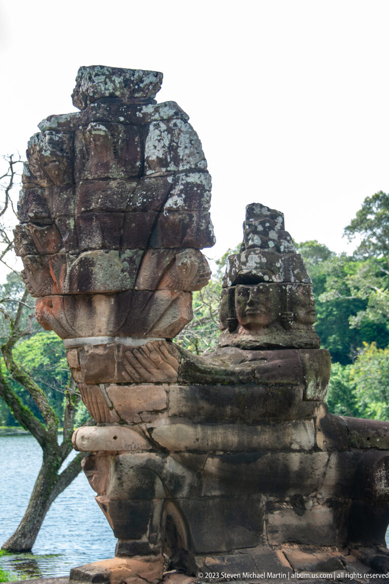 Rear oblique view of two weathered stone naga terminals extending over the moat at Angkor Thom.