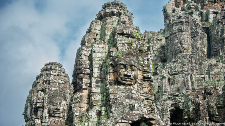 Cluster of weathered Bayon face towers rising beneath a blue sky.