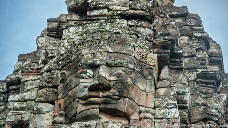 Frontal close-up of a serene carved face on a weathered Bayon tower.