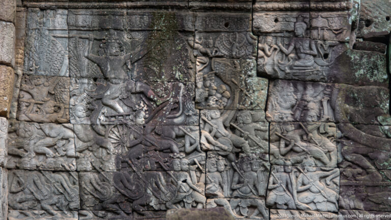 Dense Khmer bas-relief with many figures and animals carved across multiple stone blocks.