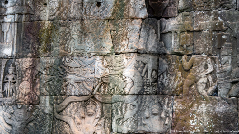 Wide Khmer narrative relief with figures and animals carved across weathered stone blocks.
