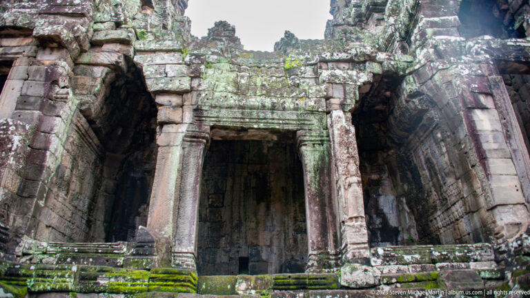 Massive weathered stone doorway leading into a dark Bayon Temple interior.