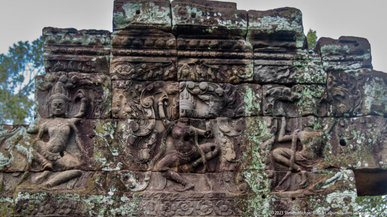 Weathered Khmer relief with a female figure, scrolling foliage, and mythic forms.