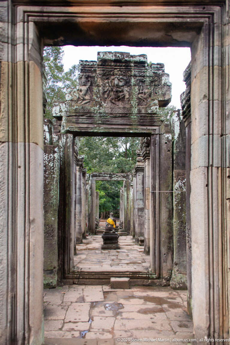 Aligned rectangular stone doorways receding through a Bayon gallery toward a distant shrine.