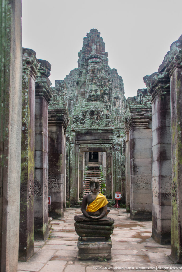 Seated Buddha in gold cloth centered within aligned stone doorways at Bayon Temple.
