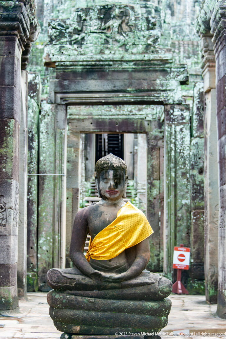Close frontal view of a seated Buddha wearing a gold sash inside a weathered stone doorway.