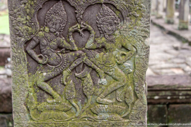 Moss-covered carved pillar with a slender female or divine figure in dense foliage.