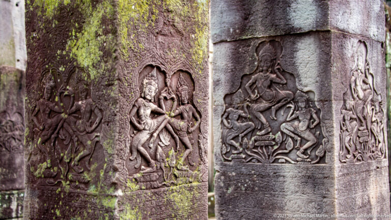 Three weathered stone pillars with separate carved relief panels of figures.