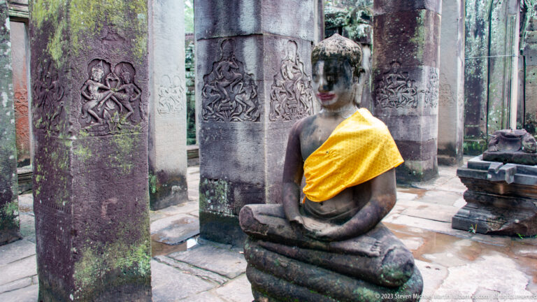Seated Buddha in gold cloth among carved stone pillars inside Bayon Temple.