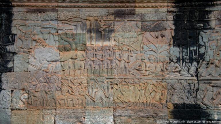 Crowded Khmer relief with marching figures, animals, and seated groups across several registers.