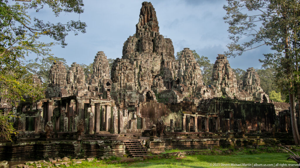 Sunlit Bayon Temple towers above a sandstone gallery and central stair.