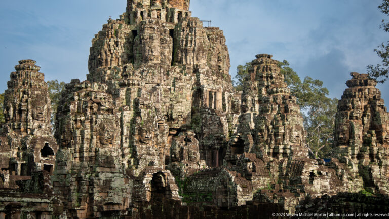 Close view of several weathered Bayon face towers with large serene carved faces.
