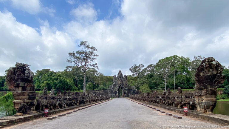 Long causeway lined with giant stone figures leading to a towered gate at Angkor Thom.