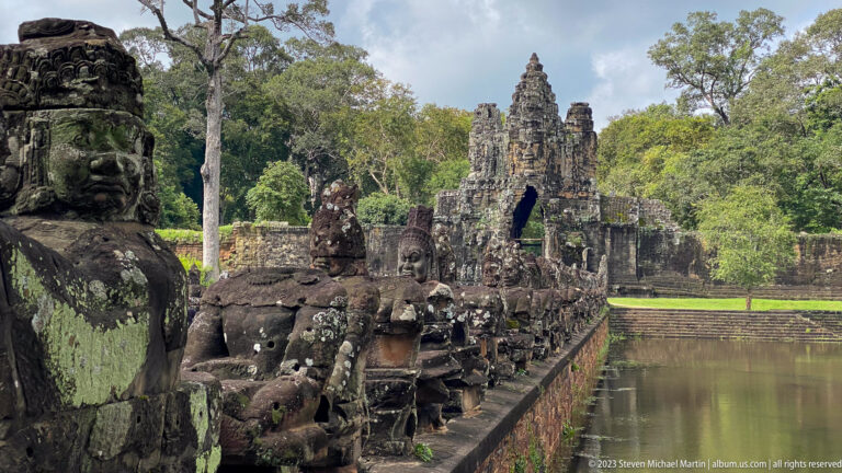 Weathered giant figures and naga balustrade beside the moat leading to an Angkor Thom gate.