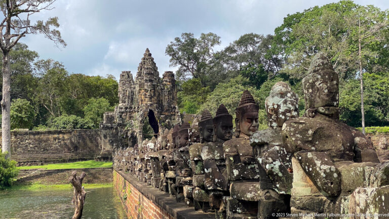 Row of crowned stone figures holding a naga balustrade beside an Angkor Thom causeway.