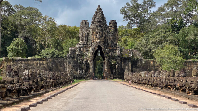 Centered road leading between stone causeway figures to a monumental face-tower gate at Angkor Thom.