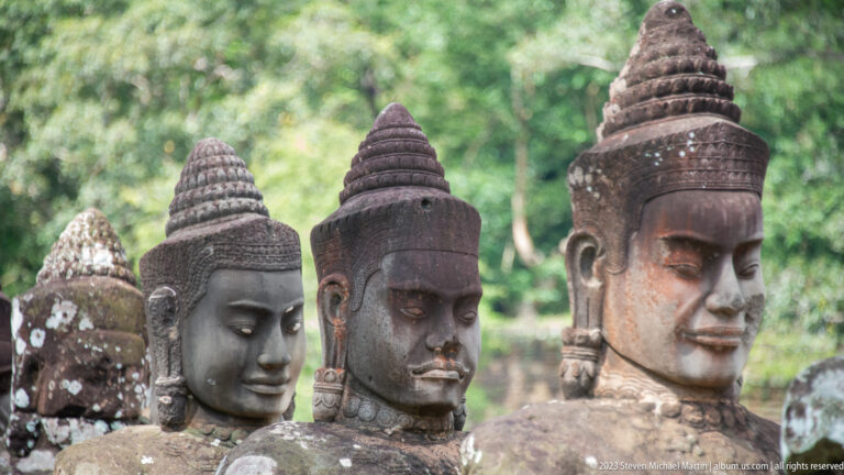 Four closely grouped sandstone guardian heads wearing tall conical headdresses against blurred forest.