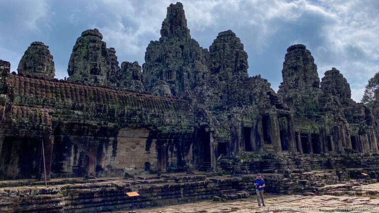Low-angle exterior view of Bayon galleries and face towers beneath dark clouds.