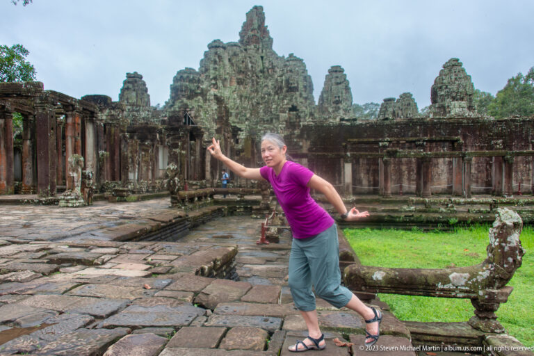 Female visitor in a magenta shirt posing in a Bayon Temple courtyard.