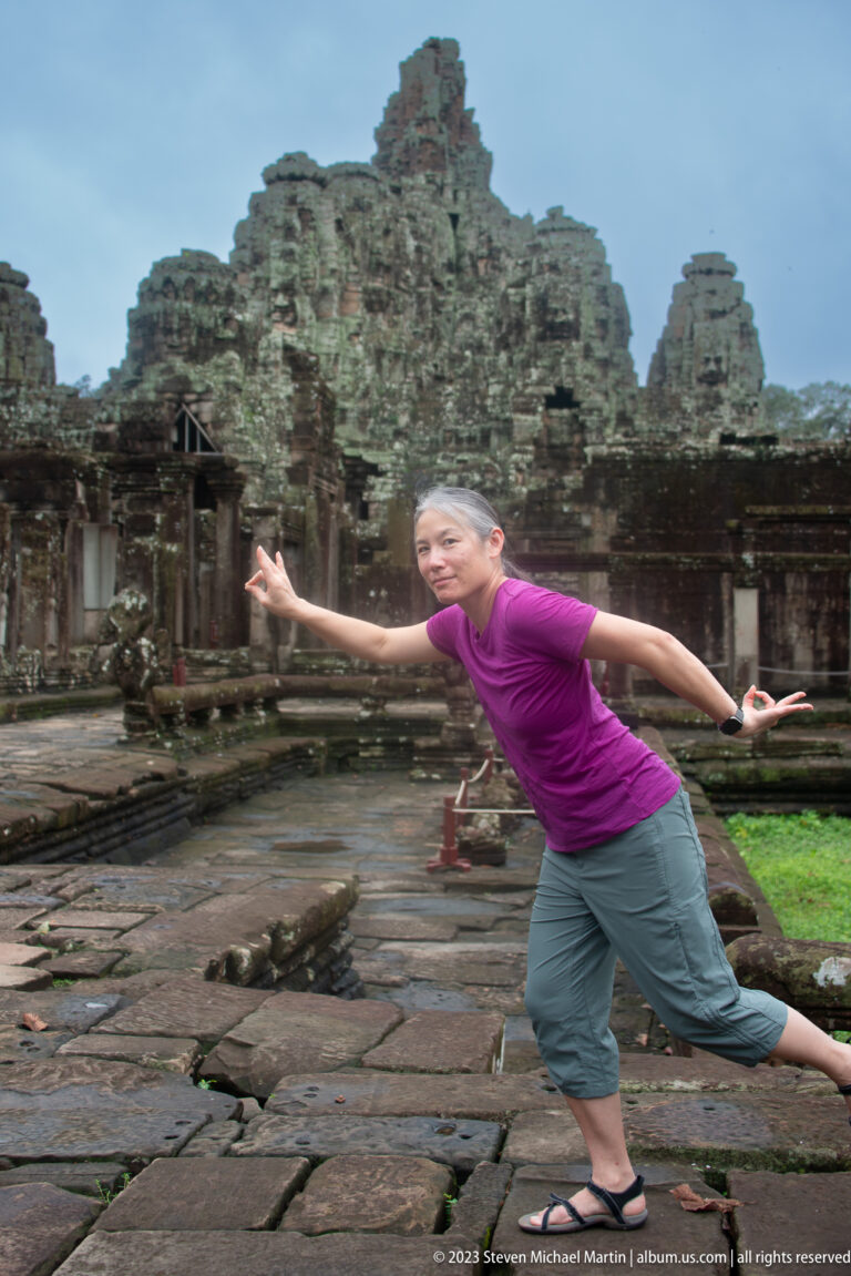 Female visitor leaning sideways with arms outstretched in front of Bayon Temple.