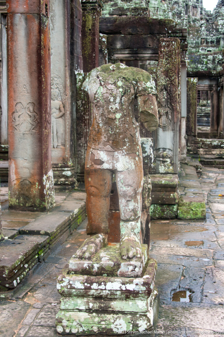 Headless weathered sandstone statue standing on a pedestal inside Bayon Temple.